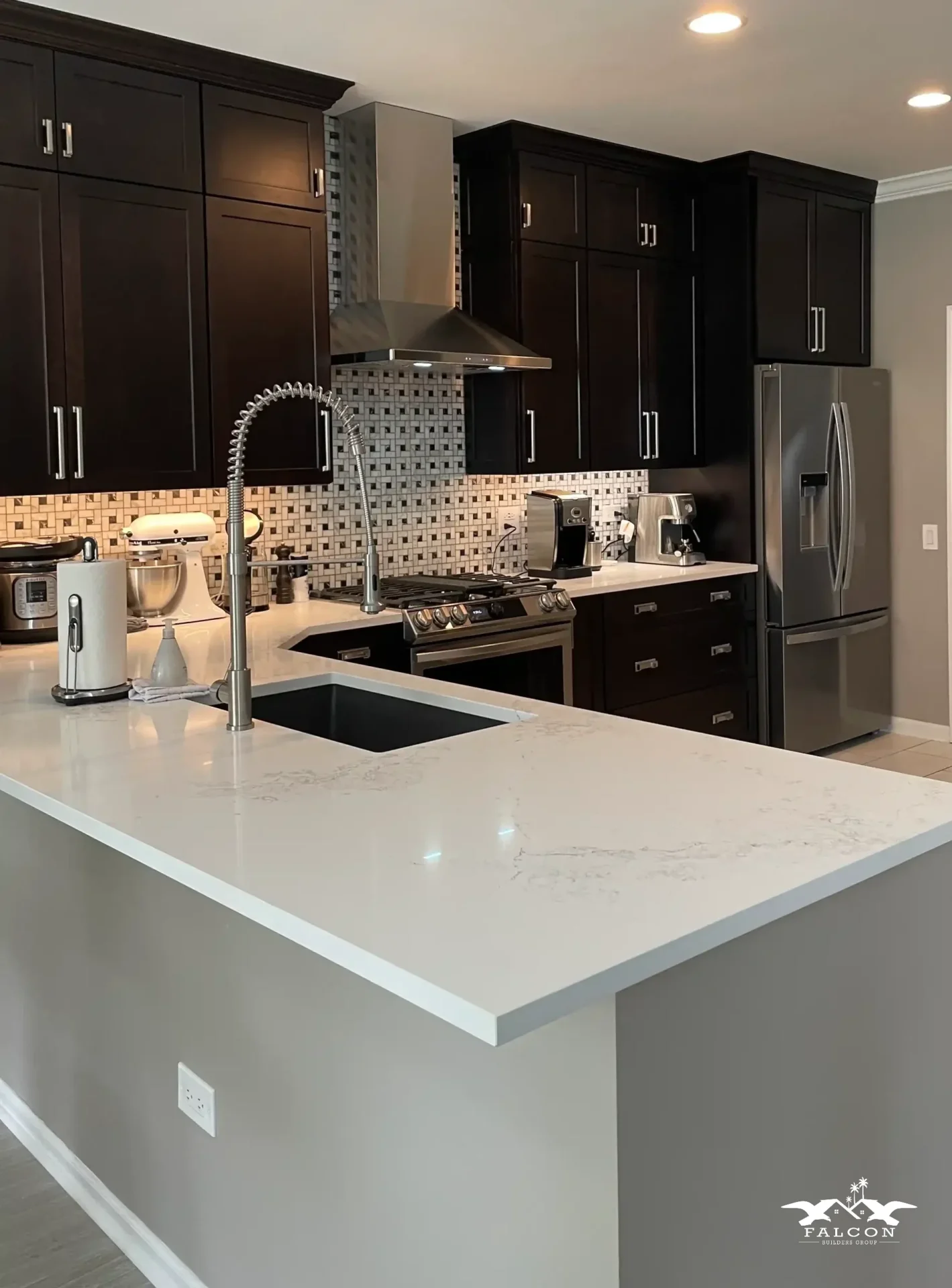 Kitchen remodel featuring dark wood cabinets, quartz countertops, stainless steel appliances, and a modern island with built-in sink and faucet.