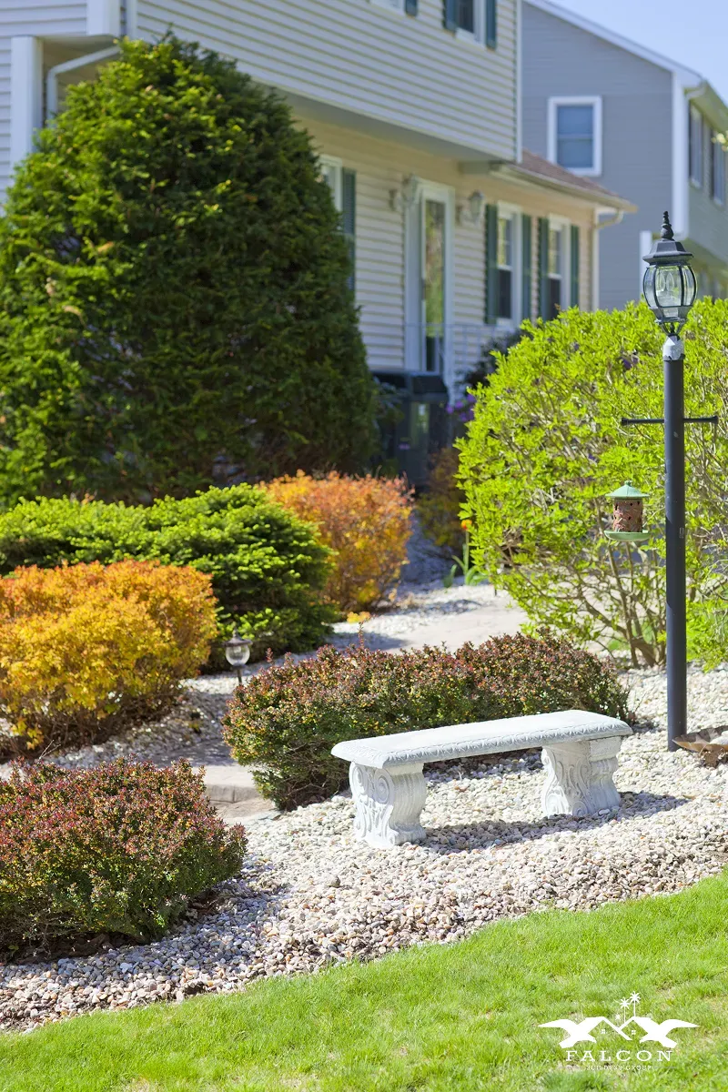 Professional landscaping service featuring manicured shrubs, decorative gravel pathway, garden lighting, and well-maintained front yard design enhancing residential curb appeal.